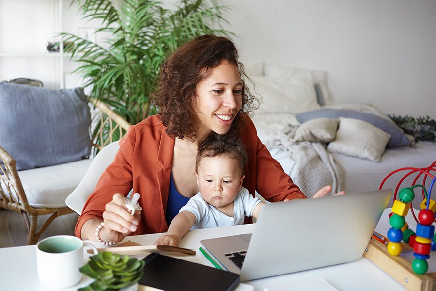 Client Center - Mother Working at Desk at Home Using Laptop, Holding Baby on Her Lap